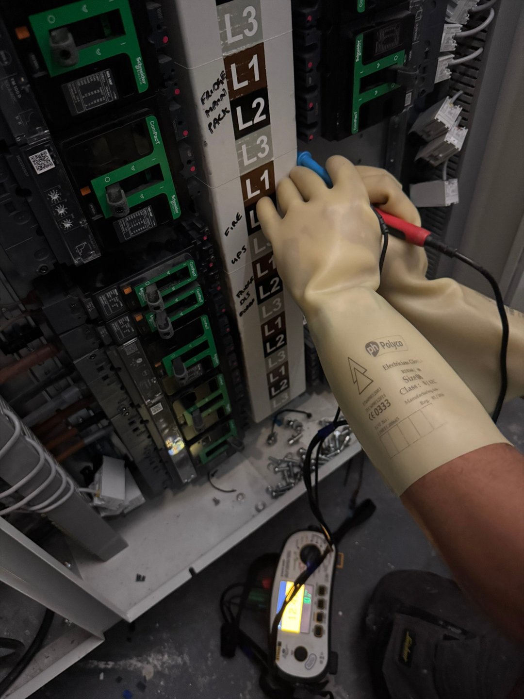 An electrician using insulated probes and a tester inside an electrical panel